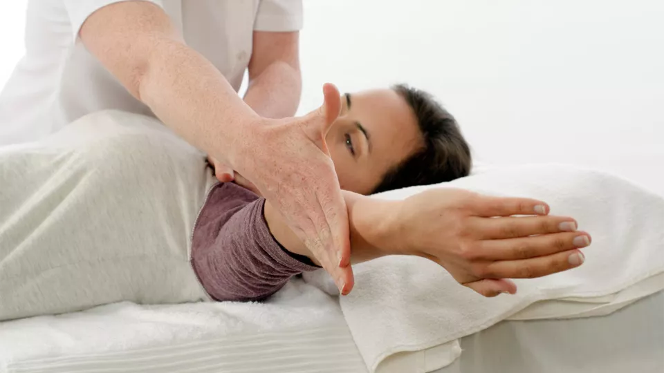 Séance pratique de kinésiologie : un thérapeute accompagne le mouvement du bras d'une patiente lors d'une formation diplômante OrTra TC.